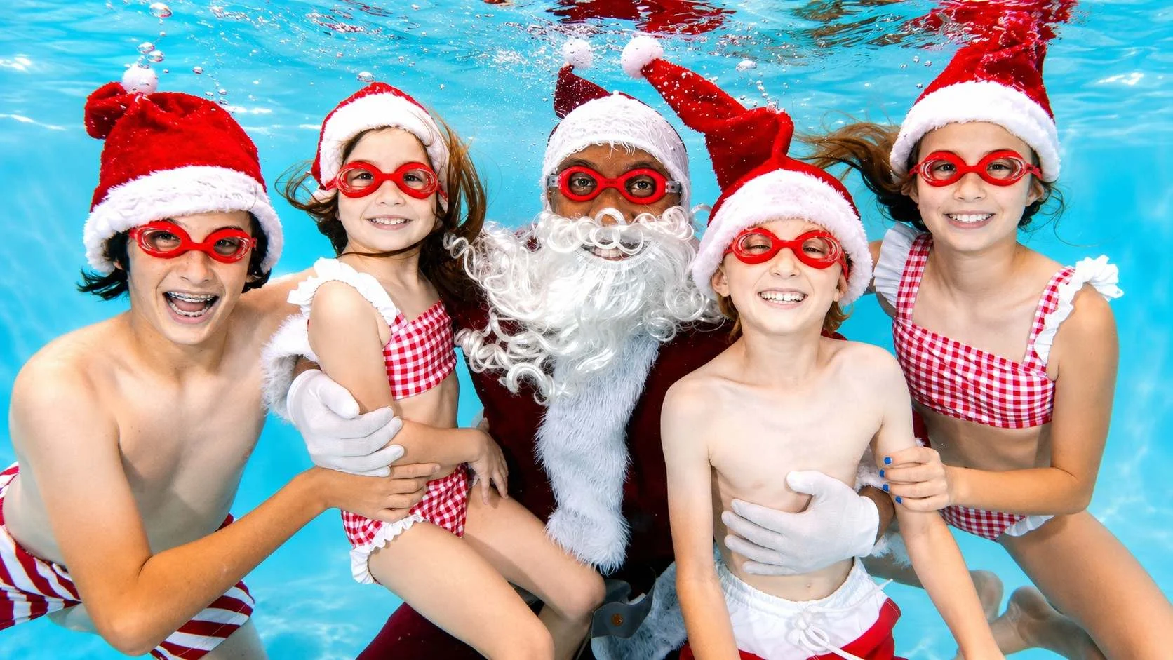 Girl posing underwater with Santa in festive goggles. Get a Kidtastics holiday photo session.